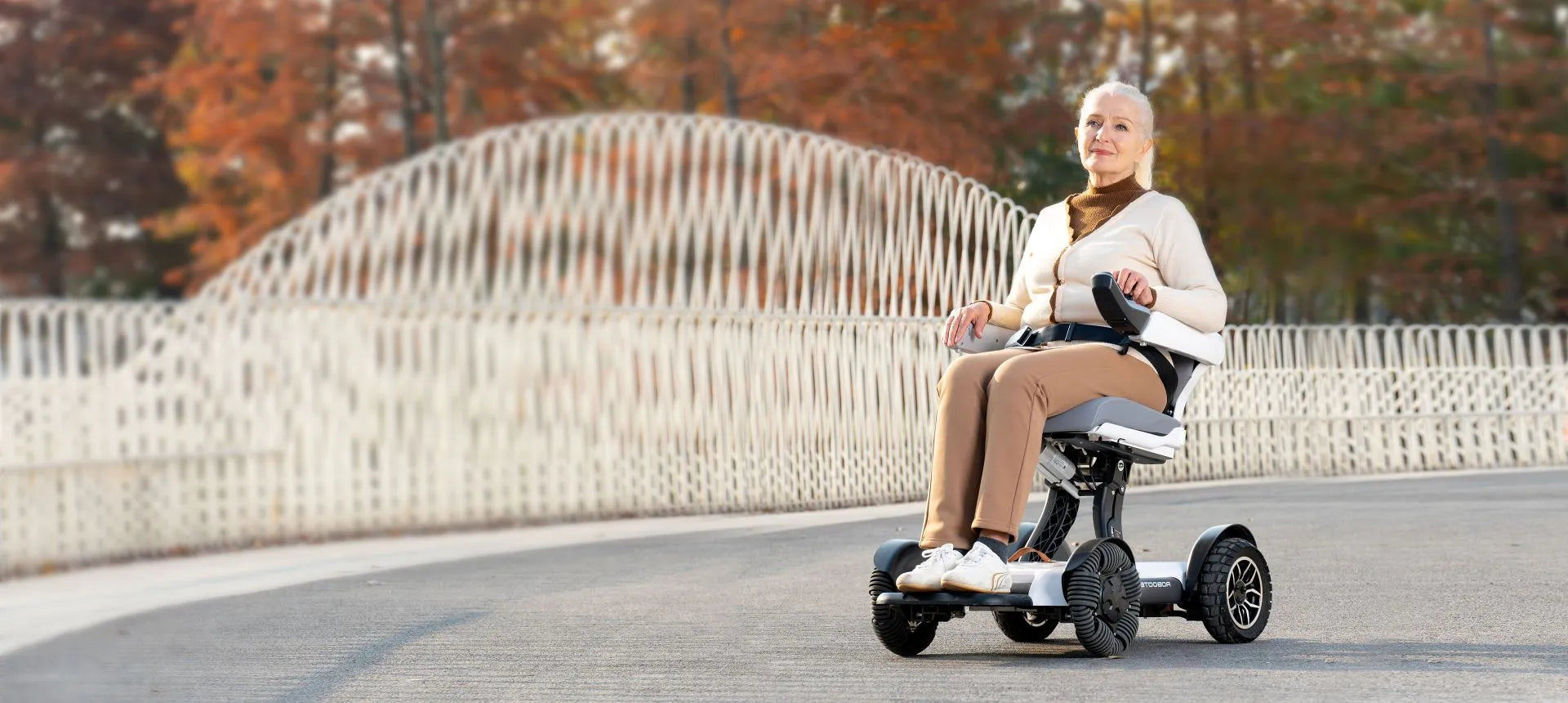 Mevrouw op een Robooter X40+ op een houten brug tussen herfstbomen